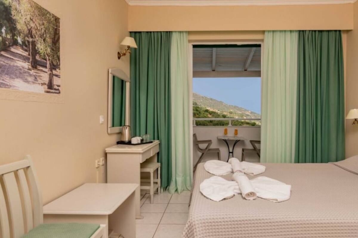 A hotel room with a bed, a desk, a chair, a small table, and a view of the outdoors.