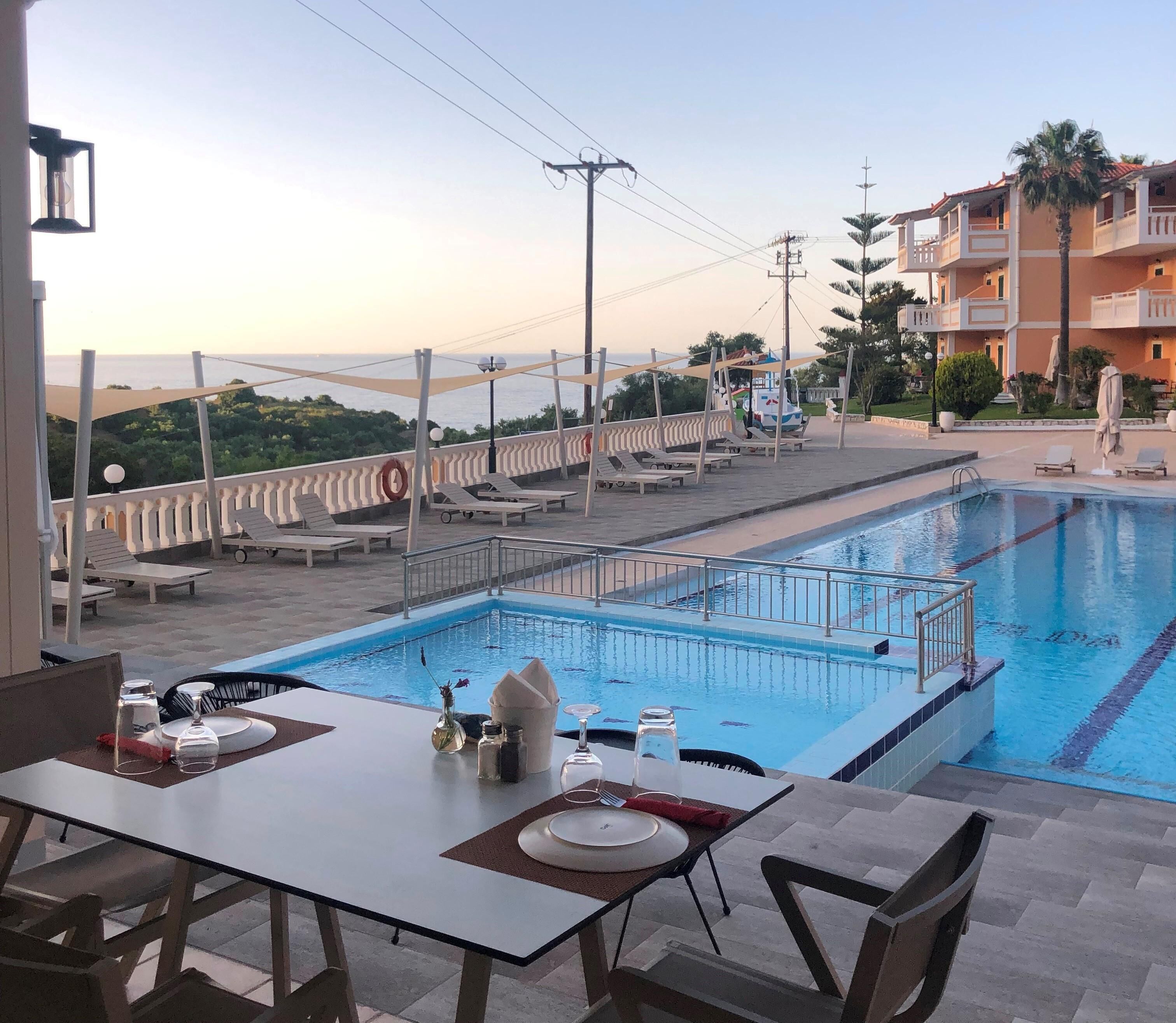 A pool area with lounge chairs and a dining table set for two, overlooking a body of water.