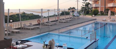 A pool area with lounge chairs and a dining table set for two, overlooking a body of water.