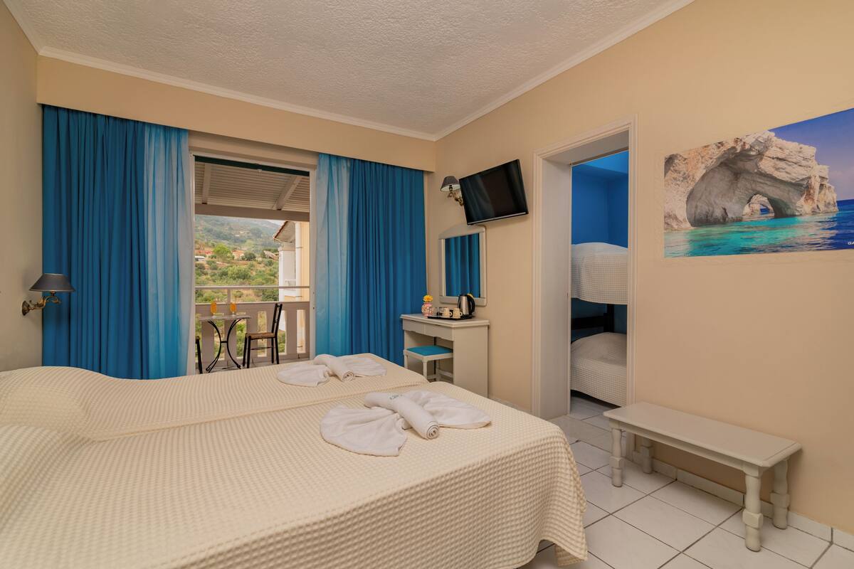 A hotel room with a bed, a desk, a chair, a TV, and a painting of a coastal scene.