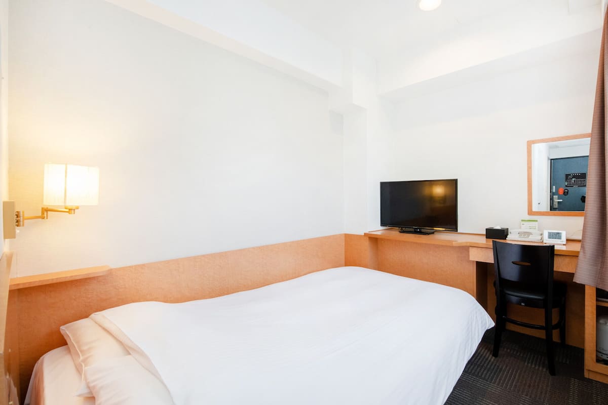 Une chambre d’hôtel avec un lit, un bureau avec un ordinateur, une télévision et un miroir.