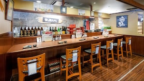 Un restaurante con barra de madera y varias sillas. Hay botellas y menús sobre la barra.