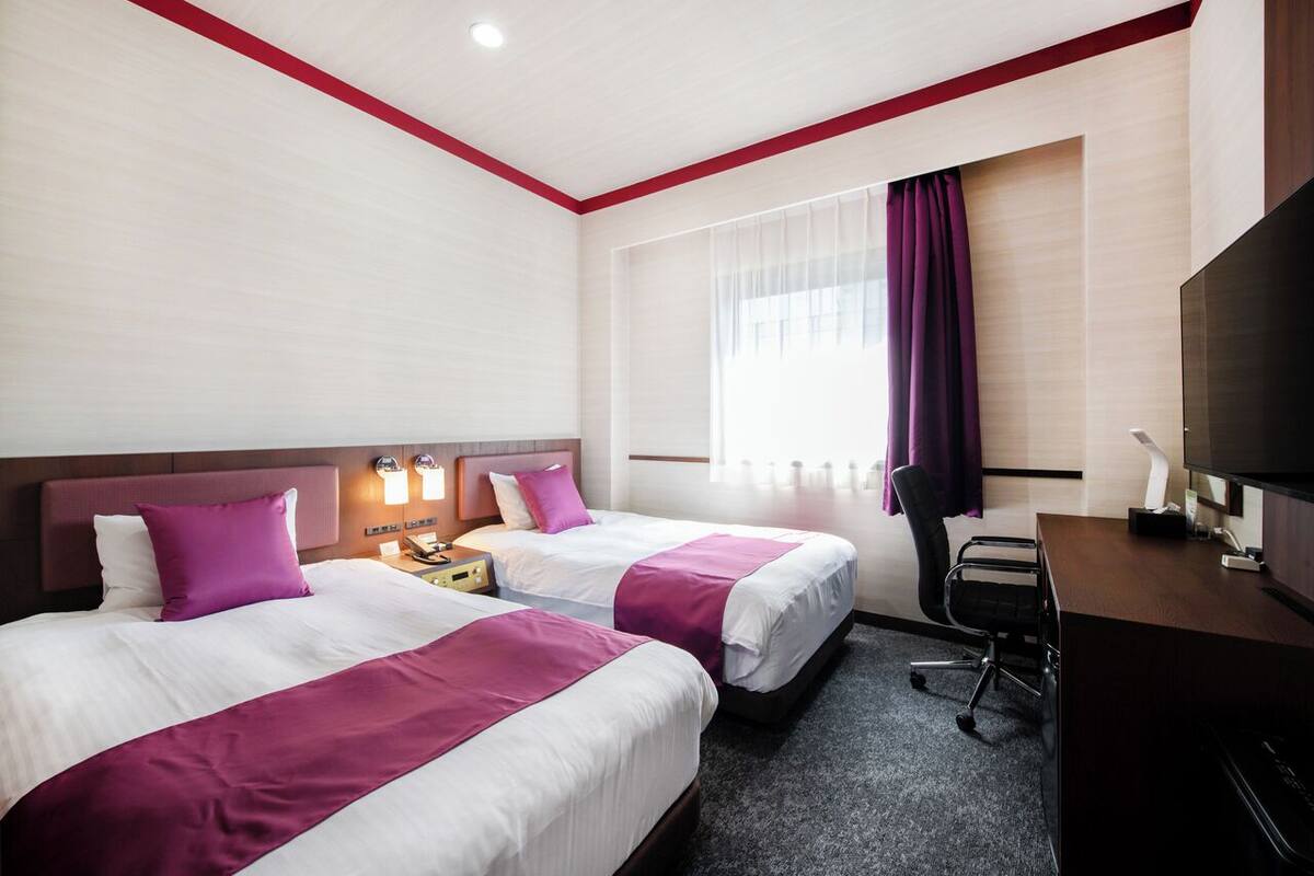 Une chambre d’hôtel avec deux lits, un bureau, une chaise et un téléviseur.