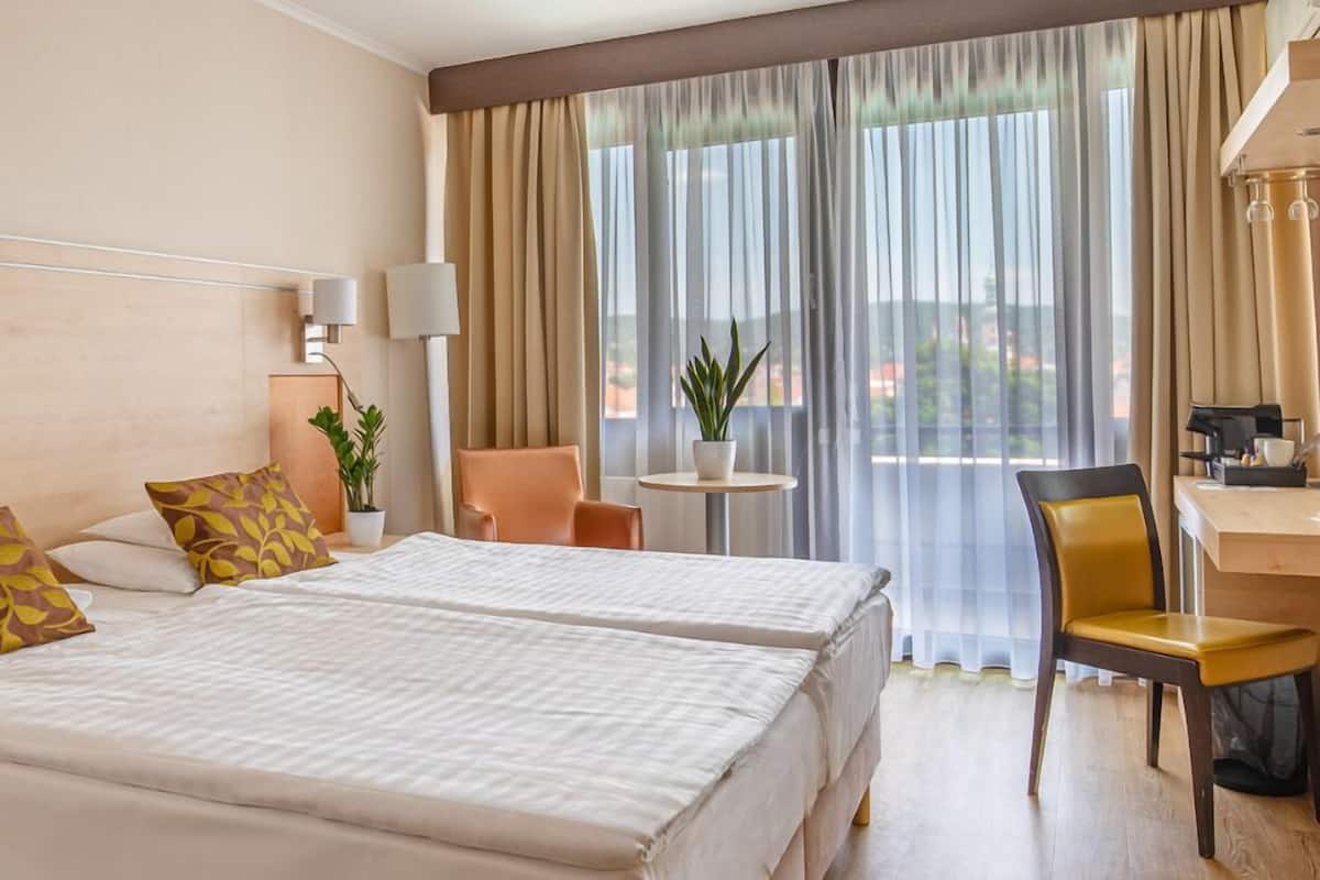 Habitación de hotel con dos camas, un escritorio, una silla, una lámpara y vista al exterior.