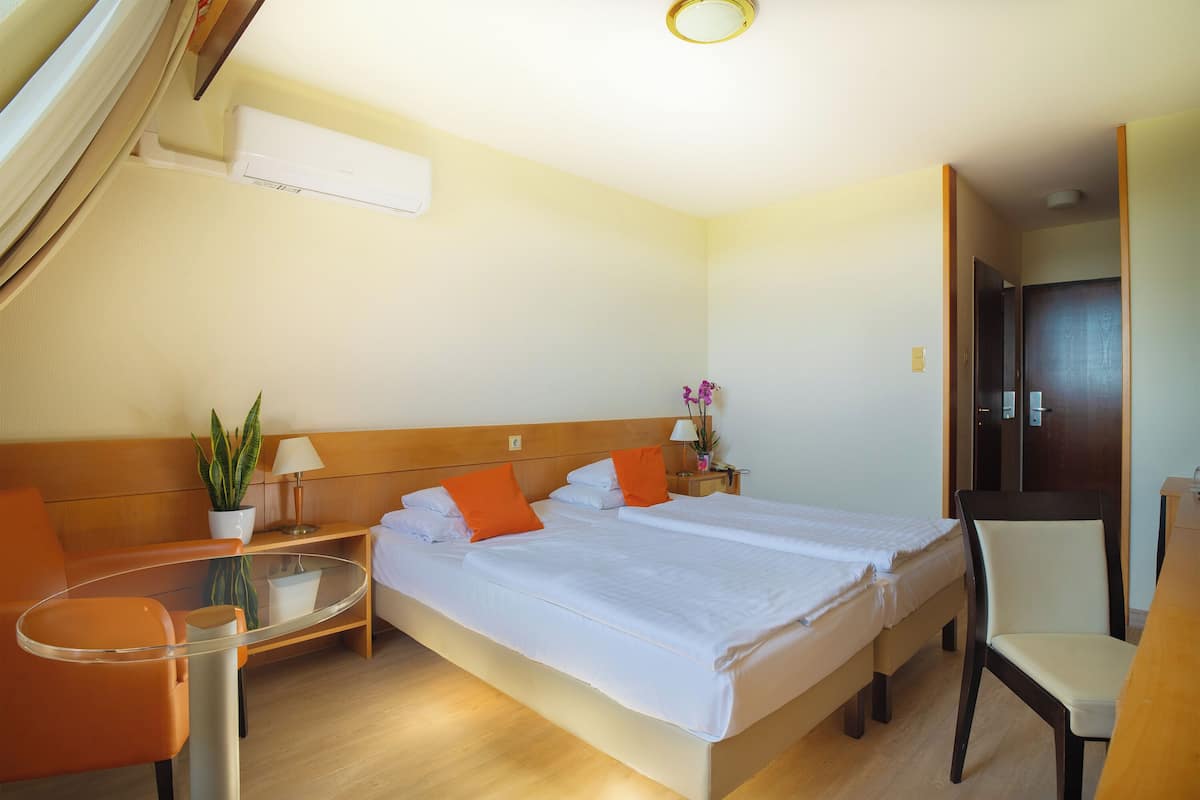 Una habitación de hotel con una cama, una silla, una mesita y una planta en maceta.