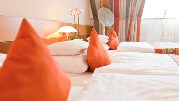 A hotel room with a bed, pillows, a lamp, and a fan.