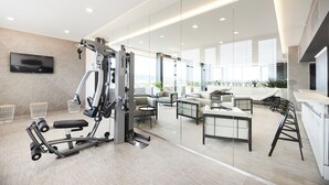 A modern gym with exercise equipment, a TV, and a seating area with a view of the city. - Hotel Sopron (Sopron)