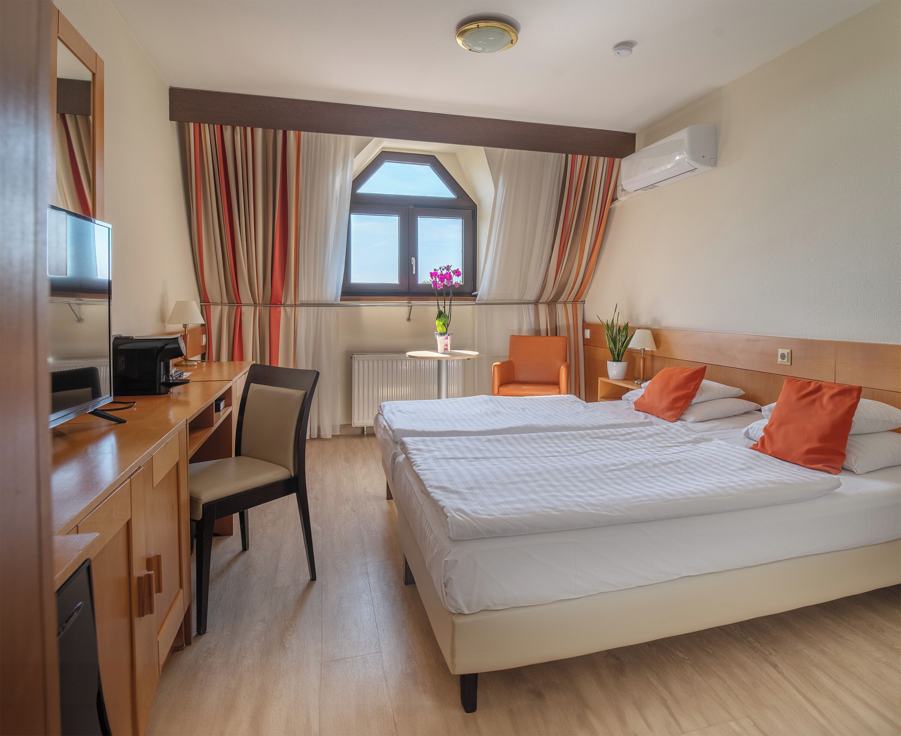 A hotel room with a bed, desk, chair, and a window with curtains.