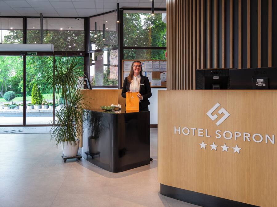 Bancada de recepção do Hotel Sopron com design moderno, uma planta em vaso e vista do exterior através de amplas janelas.