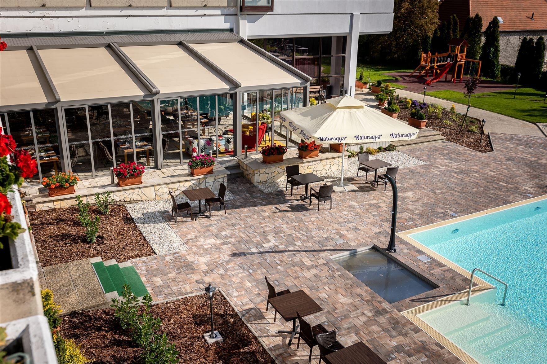 A rooftop pool area with outdoor seating and a children's play structure in the background.