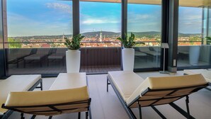 A balcony with two lounge chairs, a potted plant, and a view of a cityscape. - Hotel Sopron (Sopron)