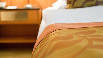 A hotel room with a neatly made bed, a bedside lamp, and a wooden nightstand.