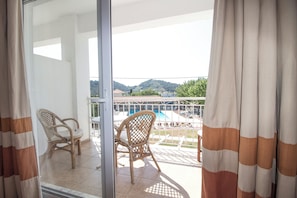 A balcony with two wicker chairs, a pool, and a view of a mountainous landscape. - Stellina Hotel (Skiathos)