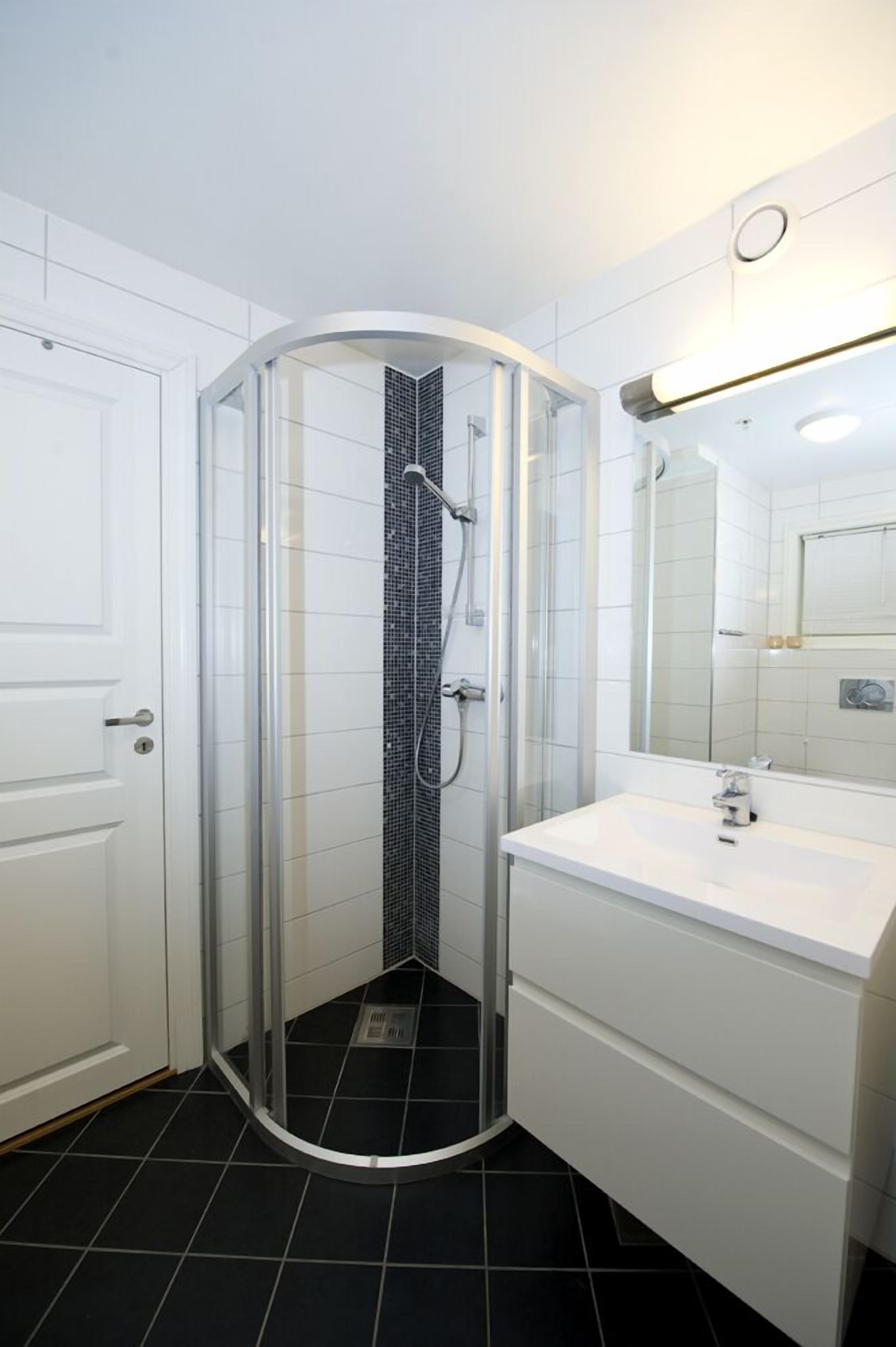 A modern bathroom with a glass-enclosed shower, white tiled walls, a white sink, and a mirror.