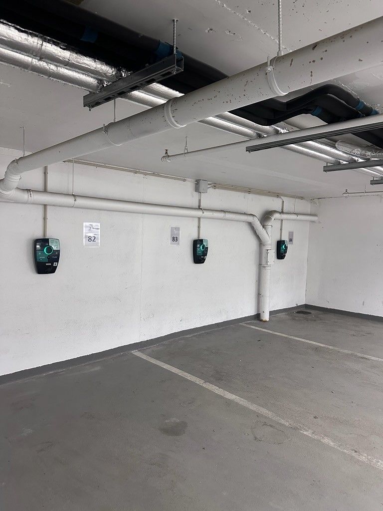 A parking garage with concrete floors, white walls, and multiple parking meters.