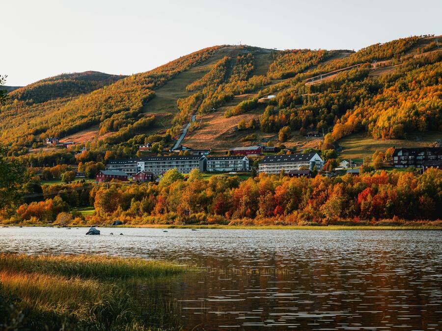 Ein Hotel am See mit mehreren Gebäuden, umgeben von Herbstlaub und Hügeln.