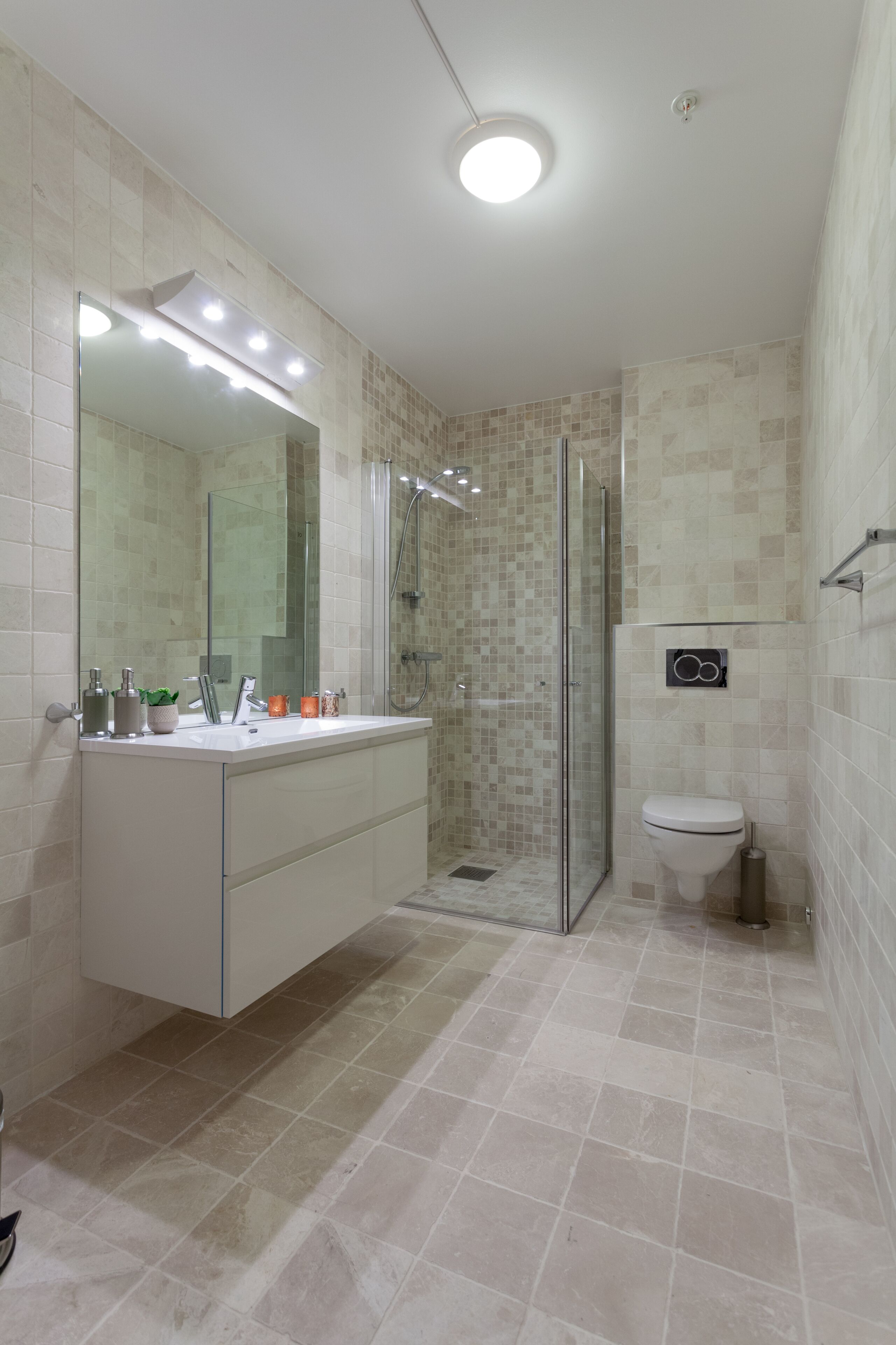 Ein modernes Badezimmer mit Duschkabine aus Glas, einem weißen Waschbecken mit Spiegel und einer Toilette.
