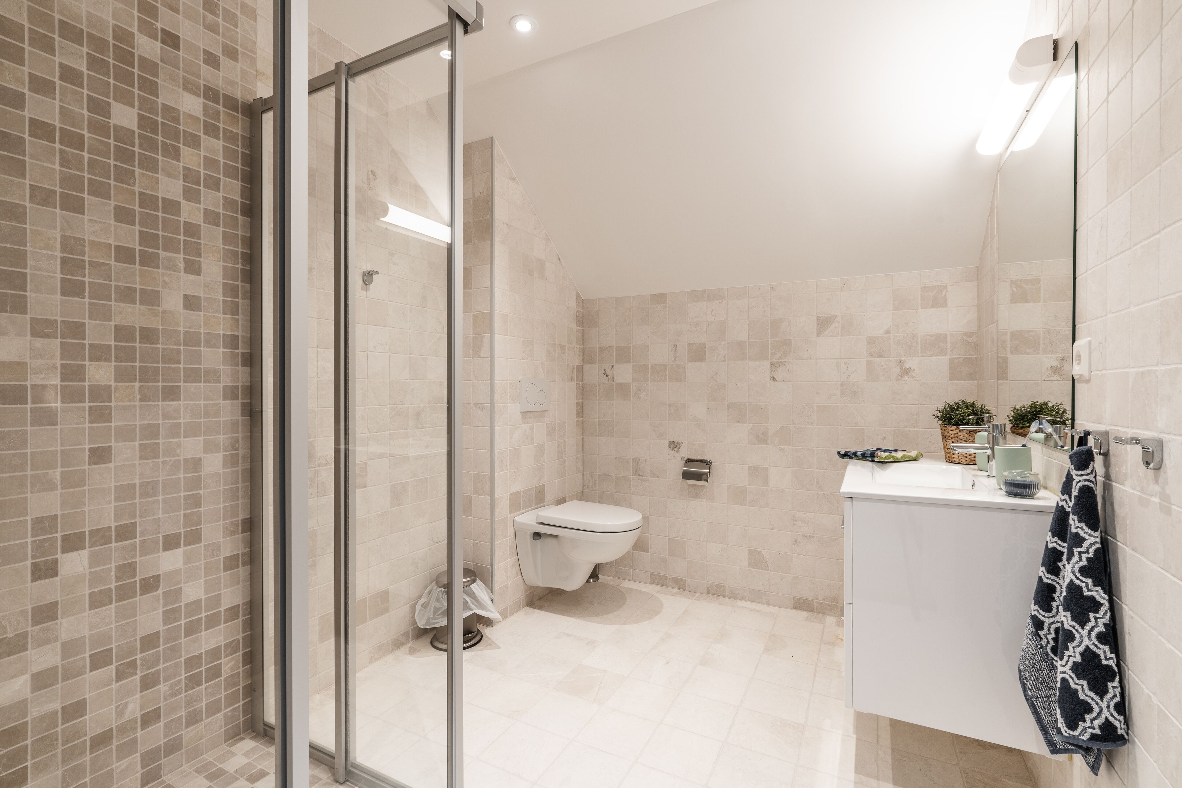 Un baño moderno con cabina de ducha de vidrio, inodoro y lavabo con una toalla colgada en la pared.