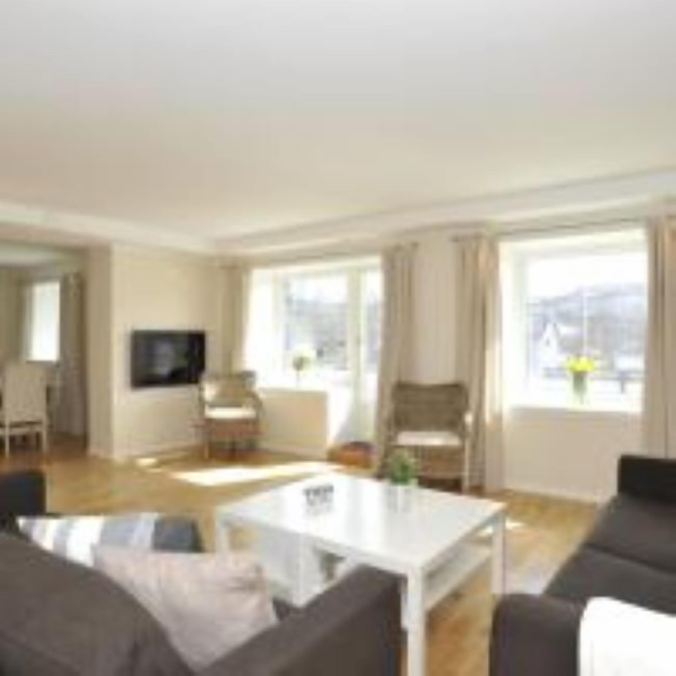 A spacious living room with a white coffee table, dark sofas, and a TV.