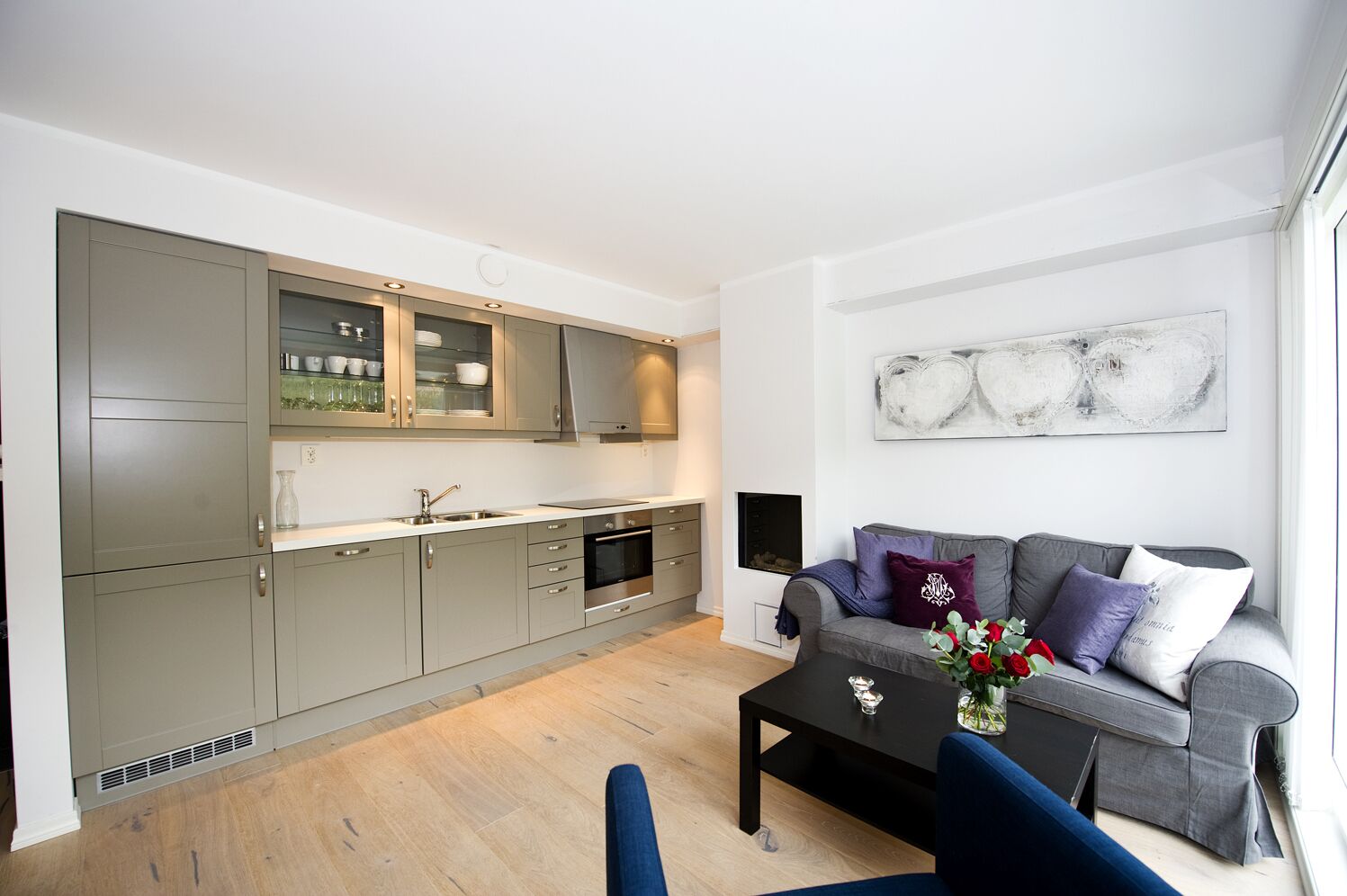 A modern kitchen with grey cabinets, a built-in oven, and a dining area with a grey sofa and a coffee table.