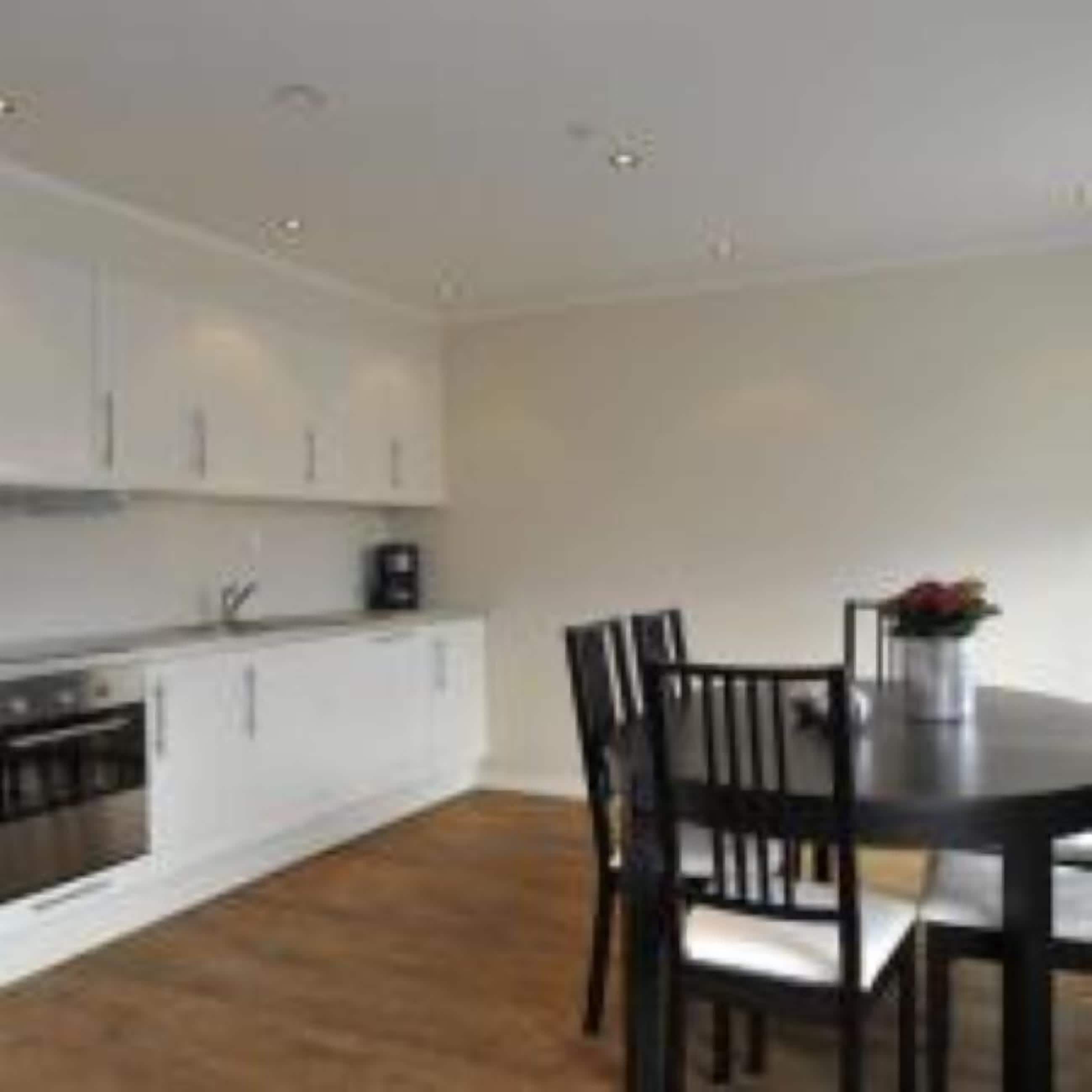 A modern kitchen with white cabinets, a black countertop, and a dining area with a dark wooden table and chairs.