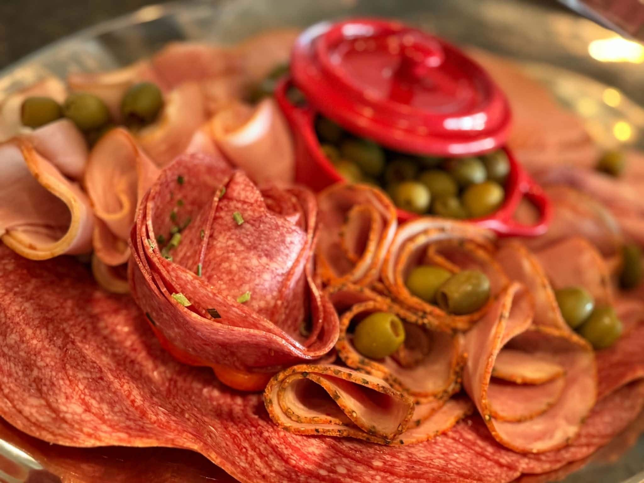 A platter with sliced meats and olives.