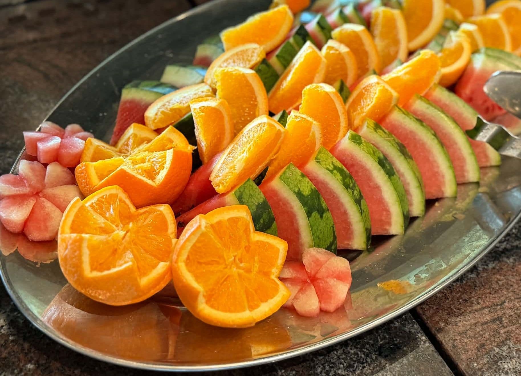 Une assiette de tranches de pastèque et d’oranges disposées sur une surface réfléchissante.