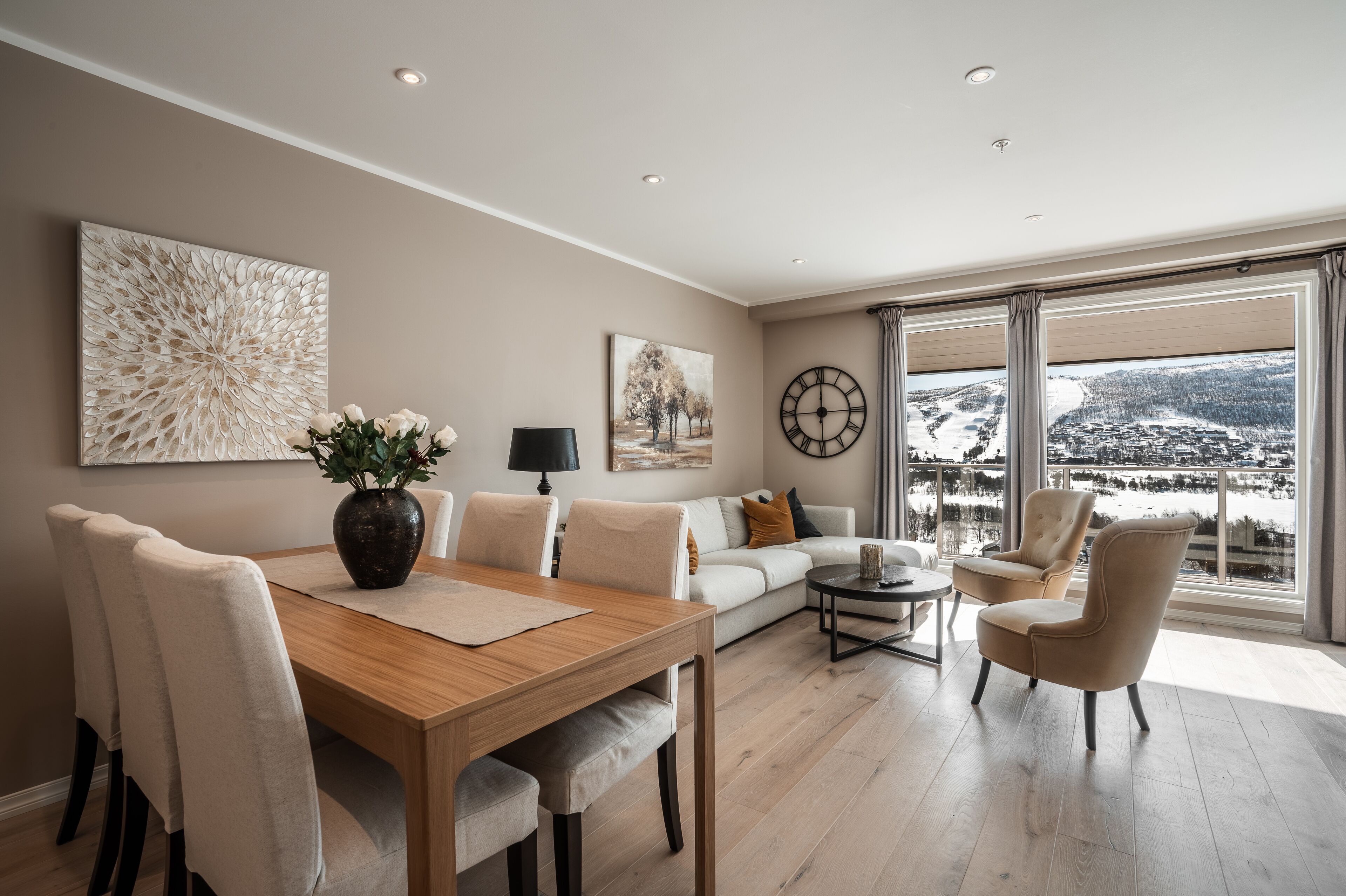 Ein modernes Wohnzimmer mit einem Holzesstisch, beigefarbenen Sofas und einem großen Fenster mit Blick auf Schnee.