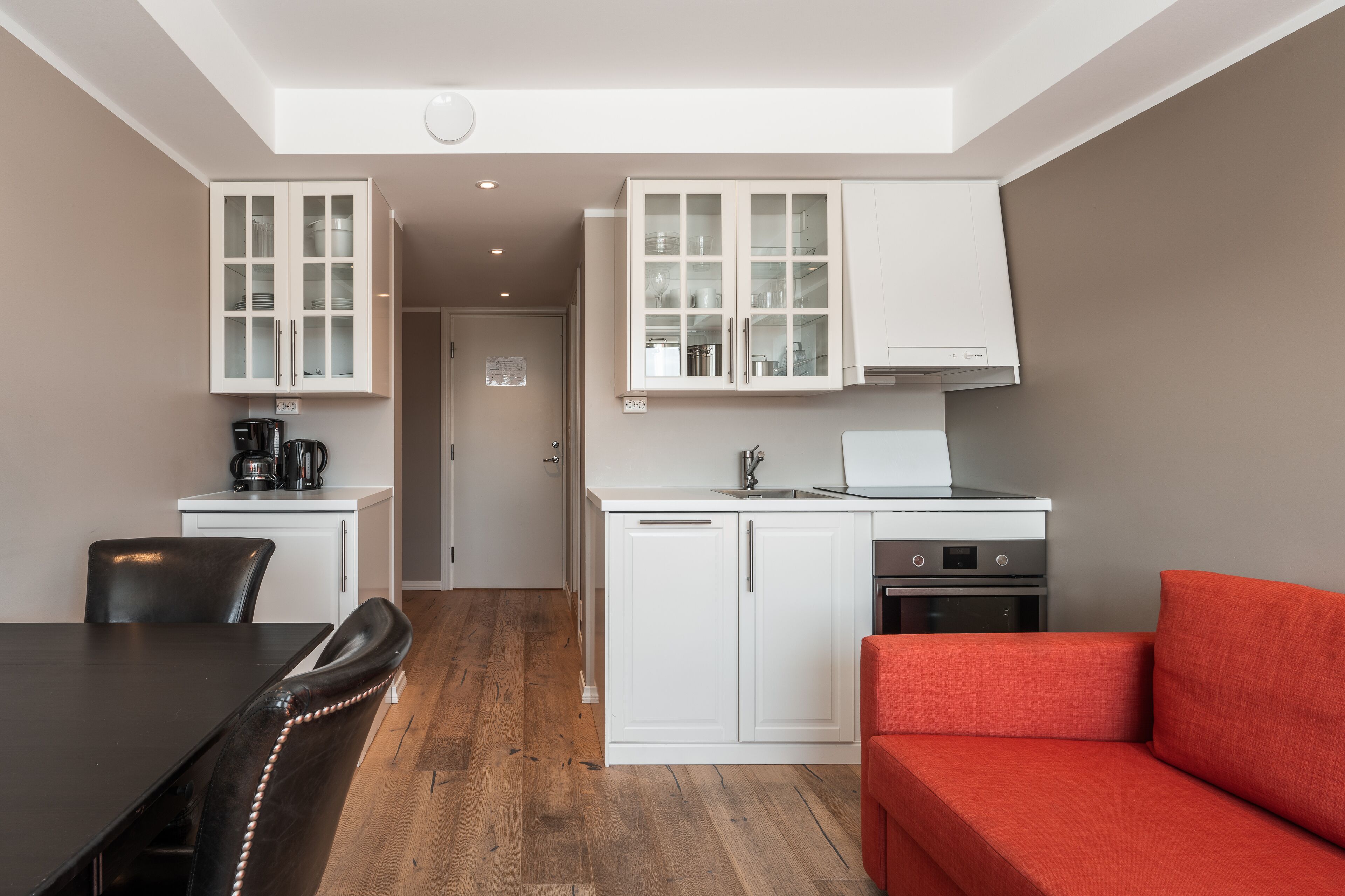 Una cocina compacta con muebles blancos, una mesa de comedor con sillas y un sofá rojo.