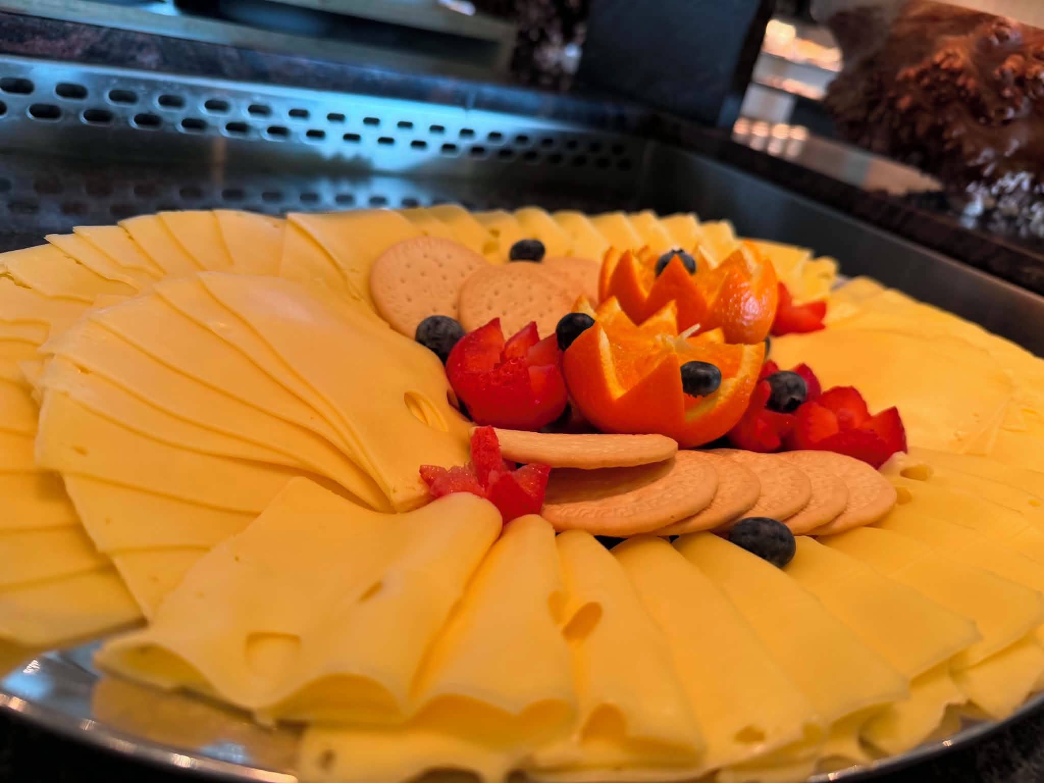 A platter of sliced cheese, crackers, and assorted fruits.