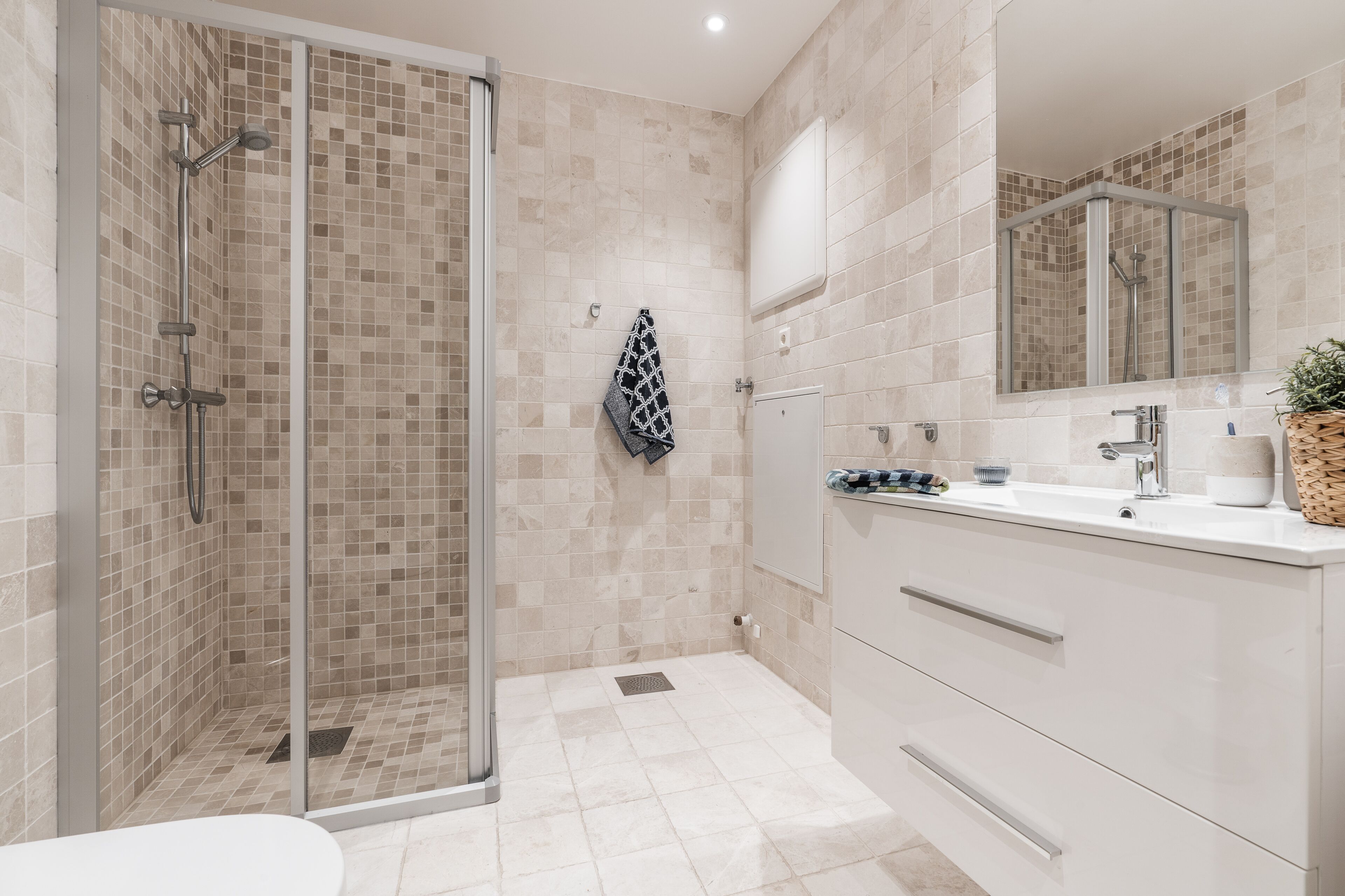 A modern bathroom with a glass-enclosed shower, a white vanity with a mirror, and beige tiled walls.