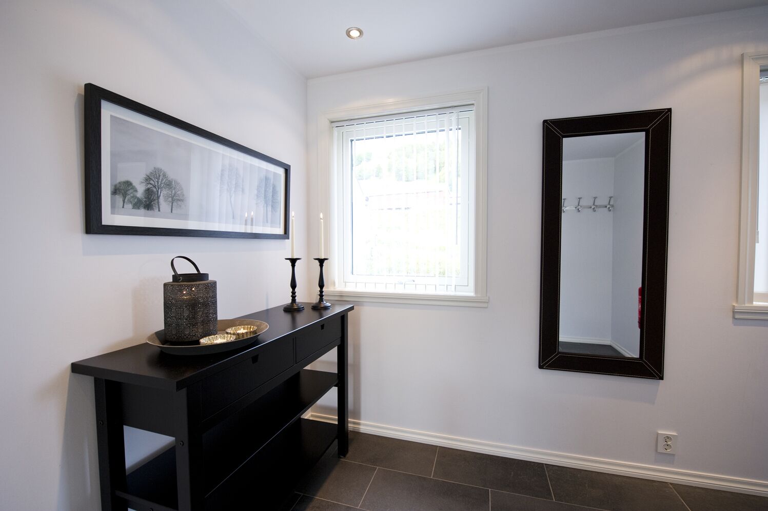 A hallway with a black console table, a framed picture, a mirror, and a window with blinds.