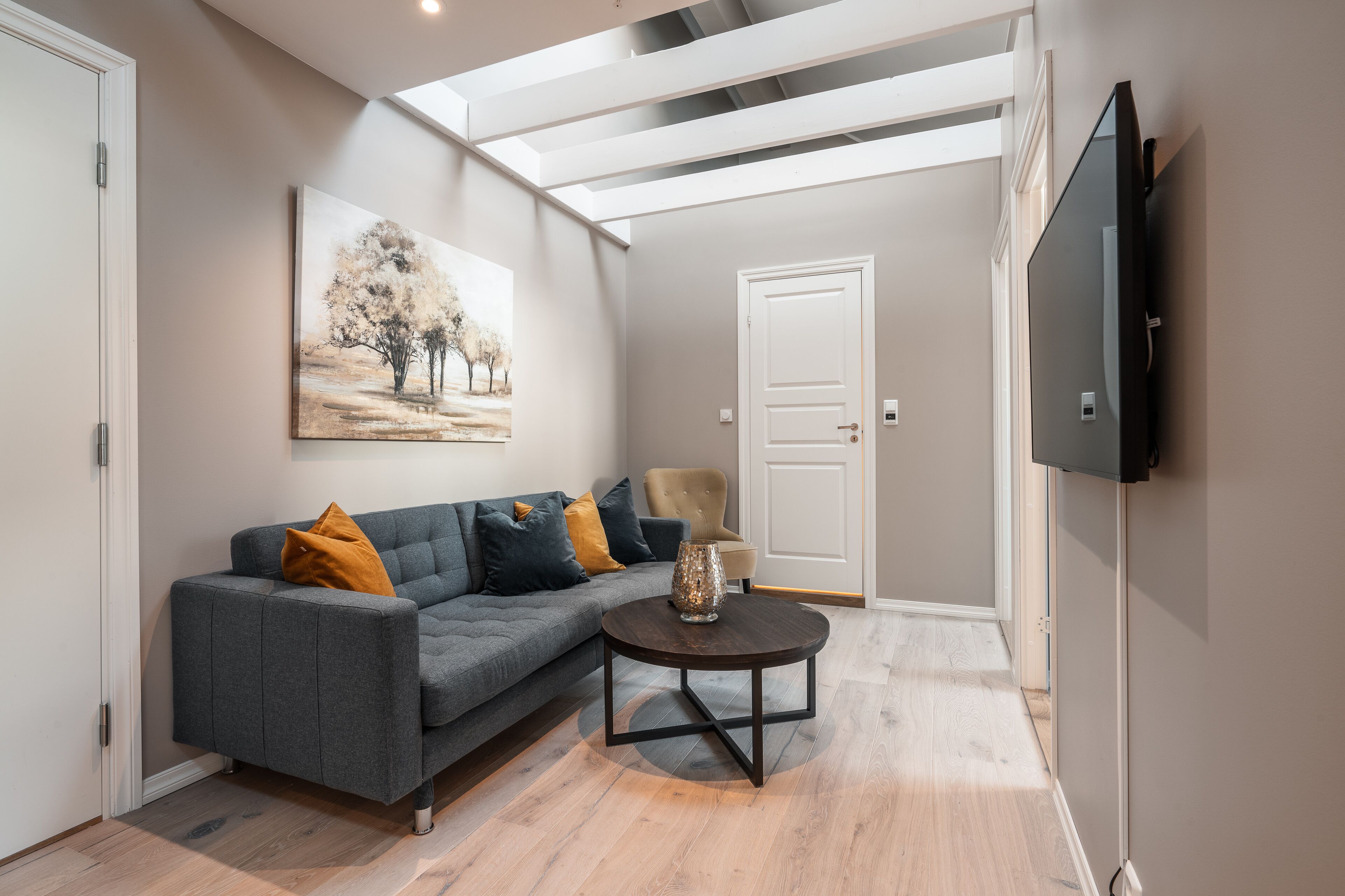 A modern living room with a grey sofa, a round coffee table, and a painting on the wall.