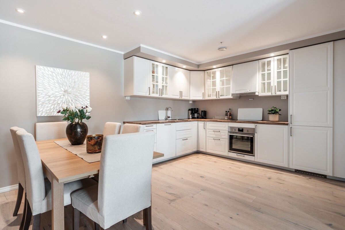 A modern kitchen with white cabinetry, a dining table with chairs, and a decorative wall piece.