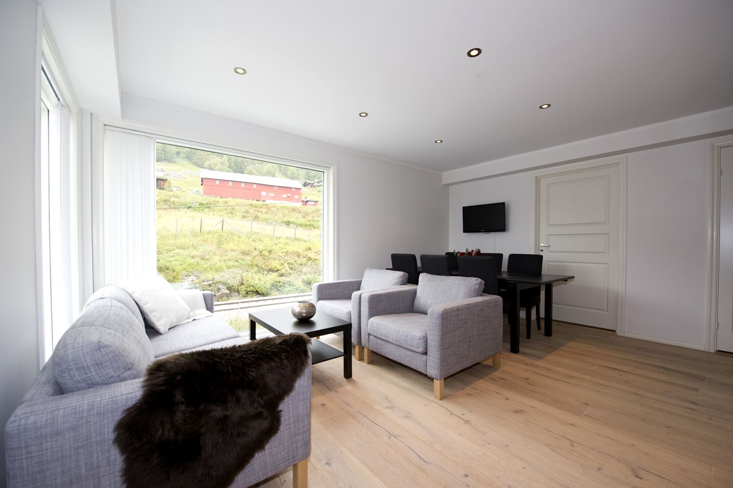 A modern living room with a large window, grey sofas, a coffee table, and a TV mounted on the wall.