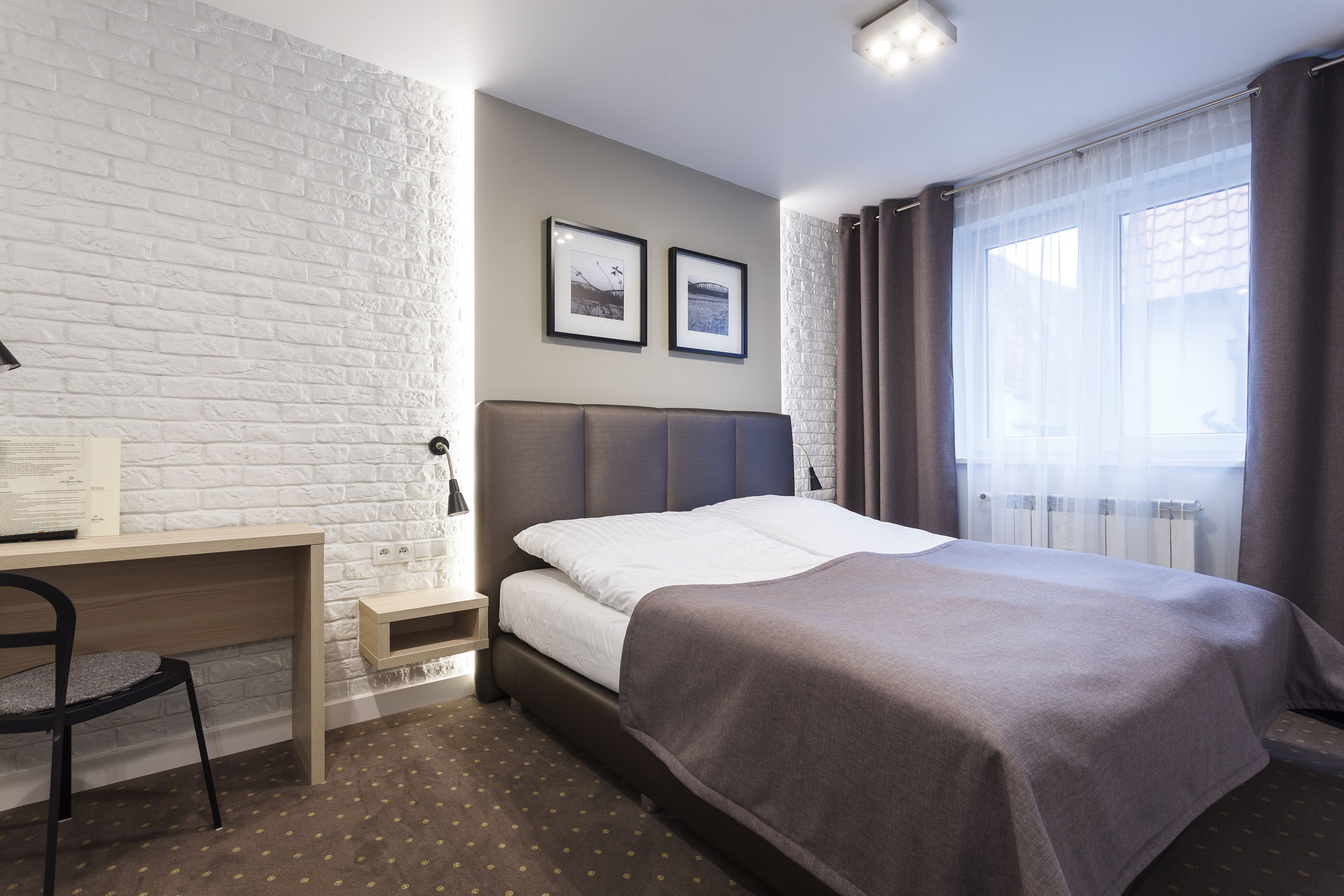Ein Schlafzimmer mit einem Bett, einem Schreibtisch, einem Stuhl und einem Fenster mit Vorhängen.