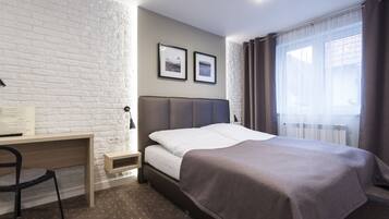 Ein Schlafzimmer mit einem Bett, einem Schreibtisch, einem Stuhl und einem Fenster mit Vorhängen.