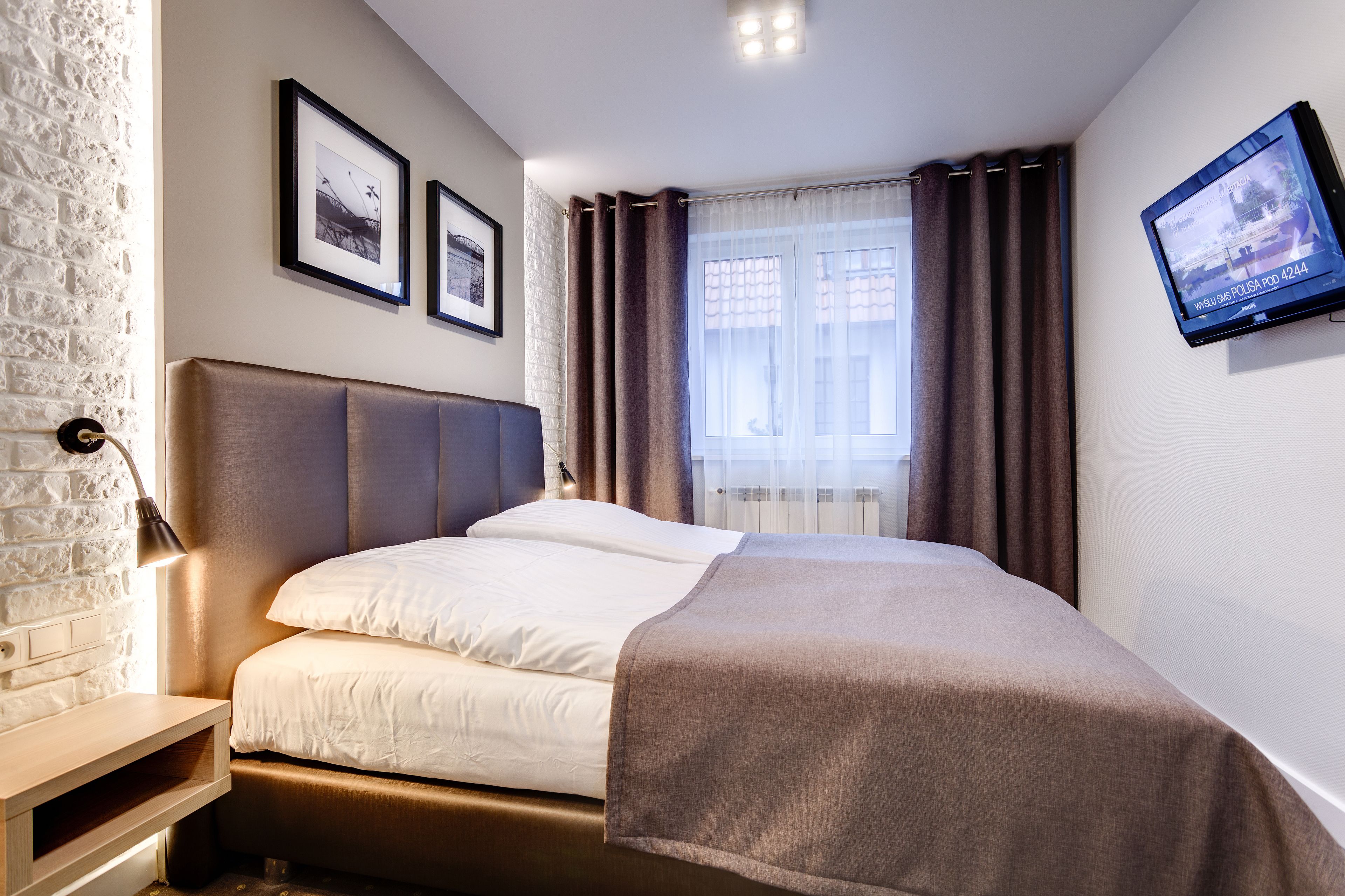 A neatly made bed with a headboard, a bedside table with a lamp, and a wall-mounted TV.