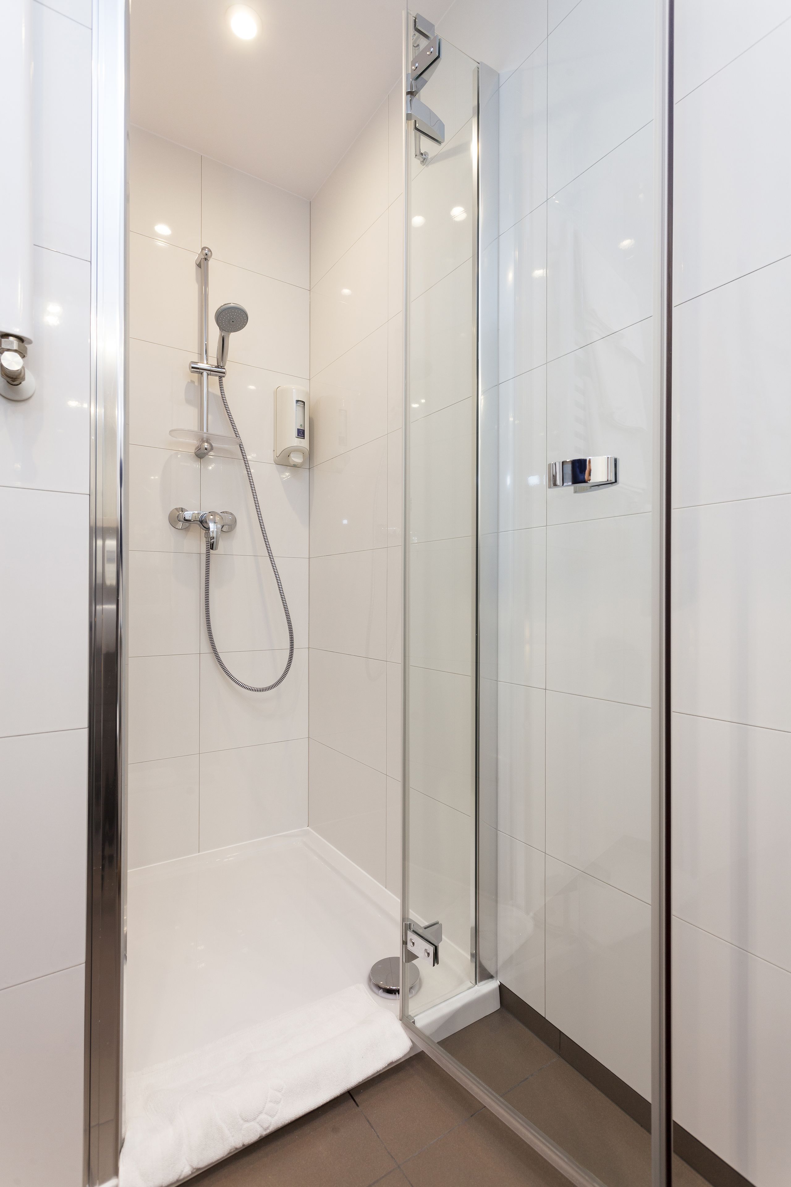 Une douche moderne dotée d’une porte en verre, d’un pommeau de douche à main et d’un panneau de commande fixé au mur.