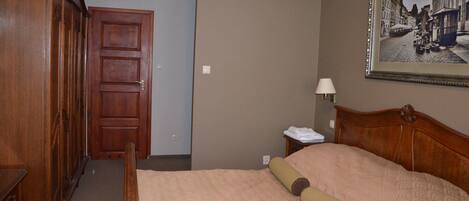 A hotel room with a wooden bed, a nightstand with a lamp, a framed picture on the wall, and a wooden wardrobe.