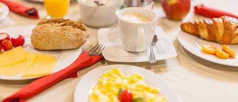 Una mesa de desayuno con platos de huevos, croissants y tostadas, una taza de café y un vaso de zumo de naranja.