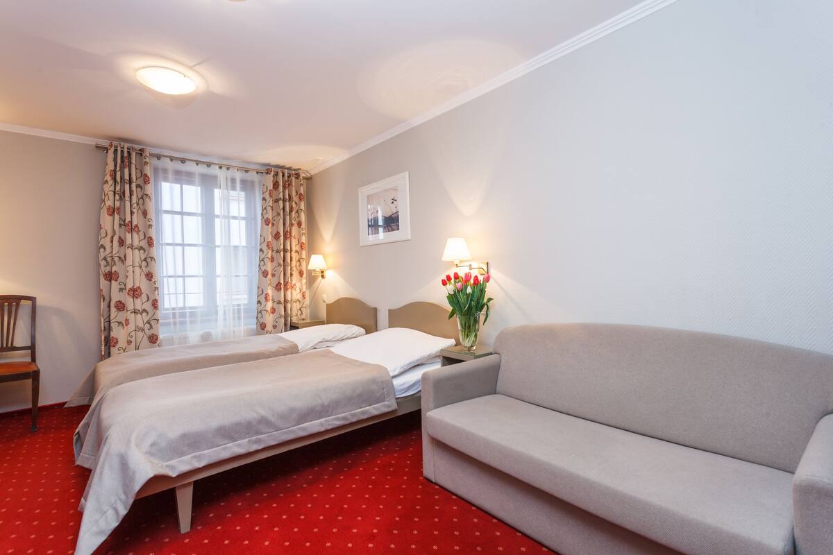 A hotel room with two beds, a sofa, a nightstand with lamps, and a framed picture on the wall.