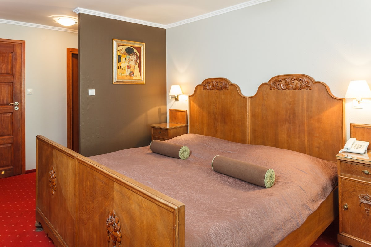A wooden bed with a headboard, two bedside tables, and a wall-mounted lamp.