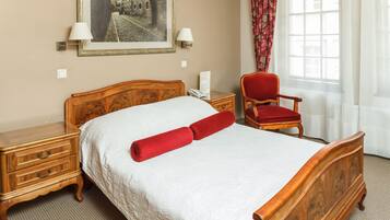 A neatly made bed with a wooden headboard, a red pillow, and a nightstand with drawers.