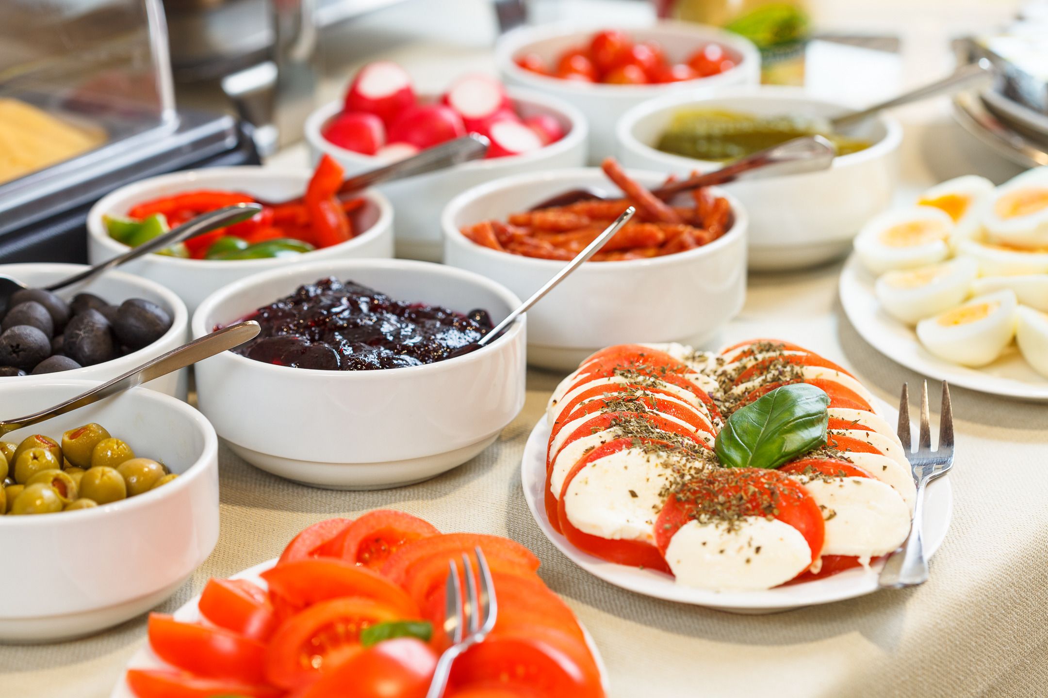 Een buffet met diverse gerechten, waaronder plakjes tomaat, olijven en een bord met plakjes mozzarella en basilicum.