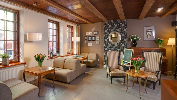 A cozy living room with wooden beams, a sofa, armchairs, a small table, and a coffee table. There are framed pictures on the wall and a window with a view. - Hotel Czarna Róża (Torun)