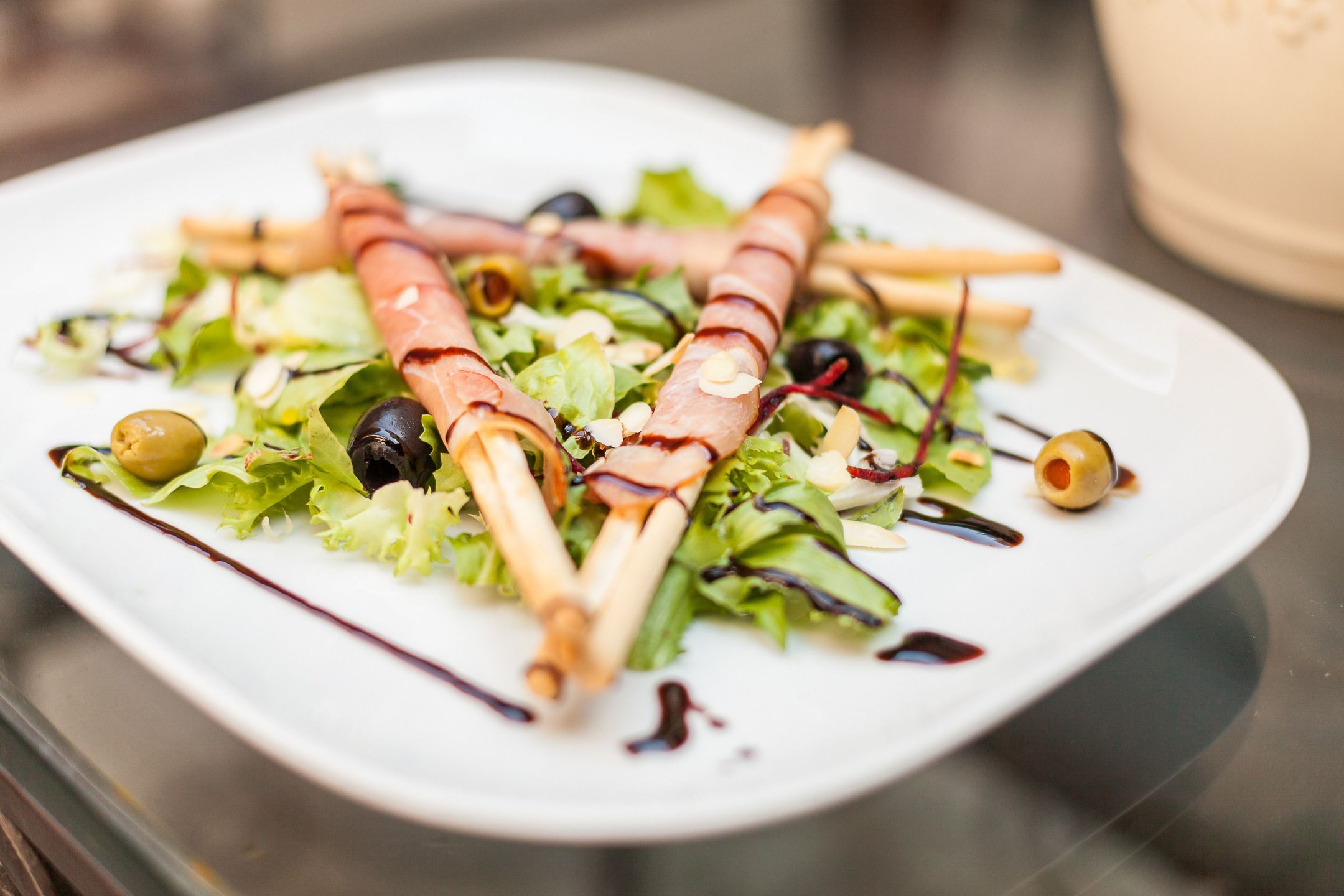 Een witte schaal met een salade met bladergroenten, olijven en in plakjes gesneden vlees.