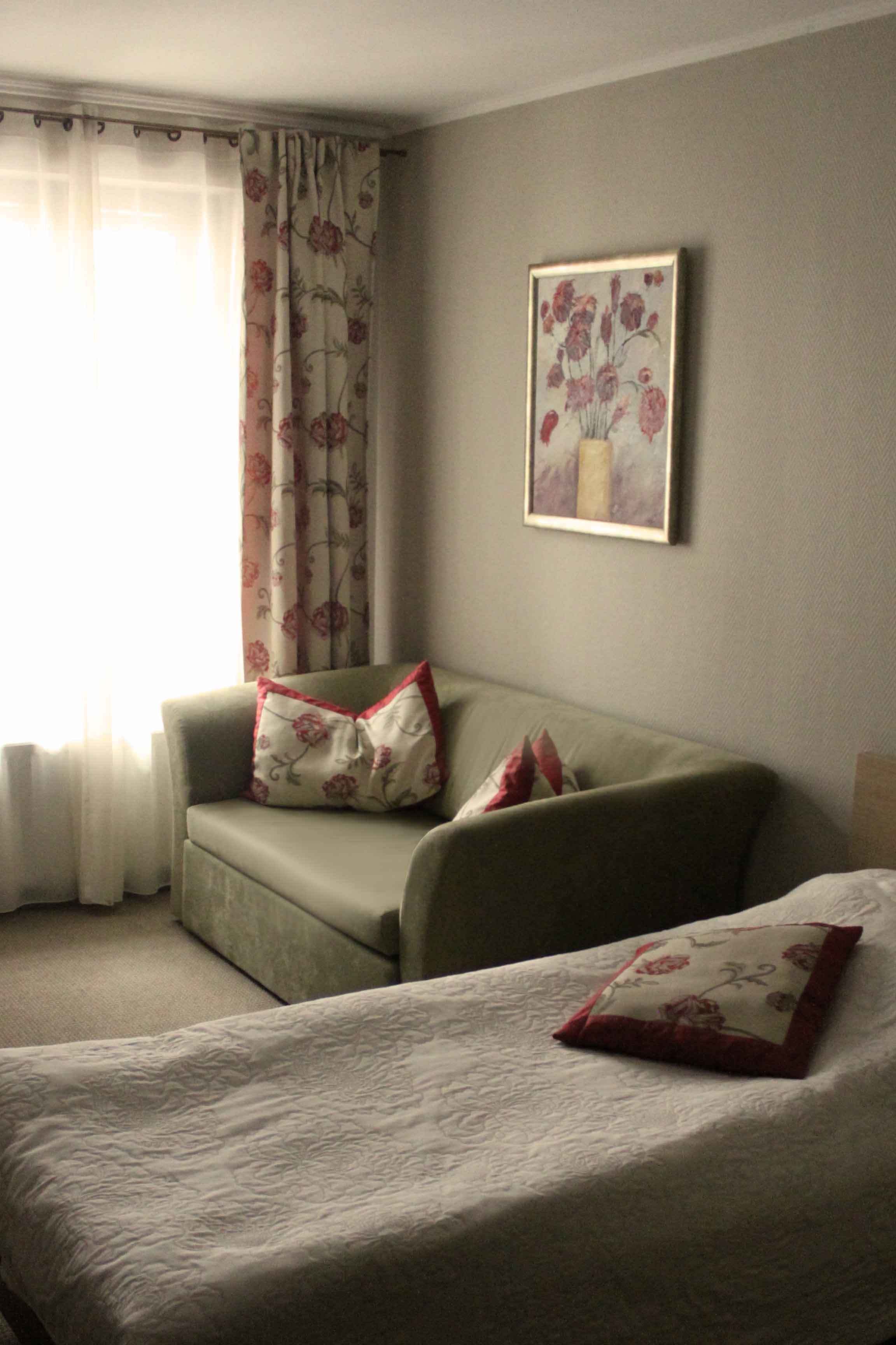 A room with a bed, a sofa, and a painting on the wall.