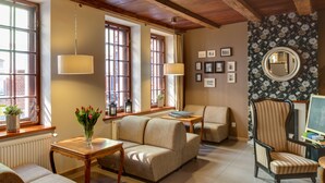 A cozy living room with a wooden ceiling, large windows, a sofa, a chair, and a table with a vase of flowers. - Hotel Czarna Róża (Torun)