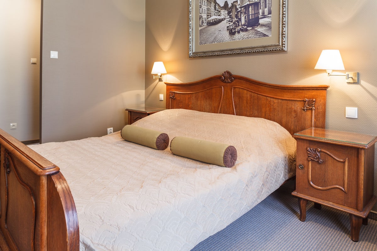 A neatly made bed with a wooden headboard, two bedside lamps, and a framed picture on the wall.